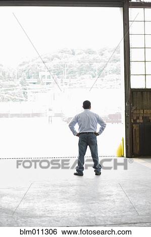 Stock Photograph - Hispanic worker standing in warehouse doorway. Fotosearch