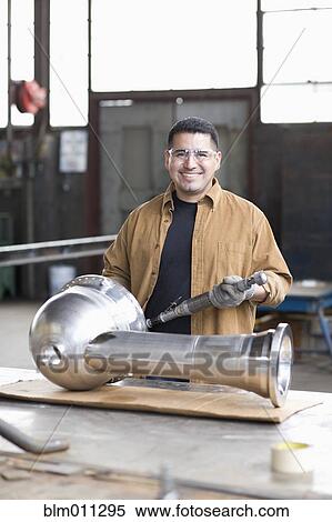 Stock Photography - Hispanic worker standing with metal pipe in warehouse. Fotosearch