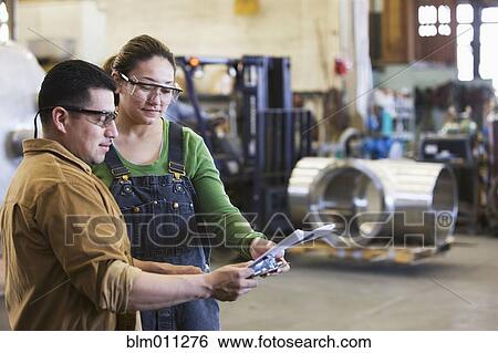 Stock Photograph - Hispanic workers reviewing paperwork in factory. Fotosearch
