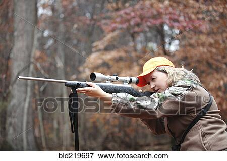 Stock Photo - Hunter in camouflage aiming rifle in forest. Fotosearch