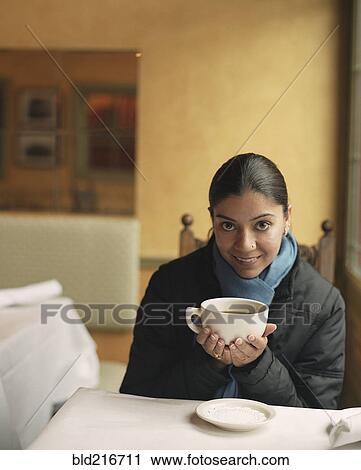 Stock Image - Indian woman drinking coffee in cafe. Fotosearch