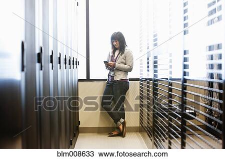 Stock Image - Japanese businesswoman using cell phone in office technology room. Fotosearch