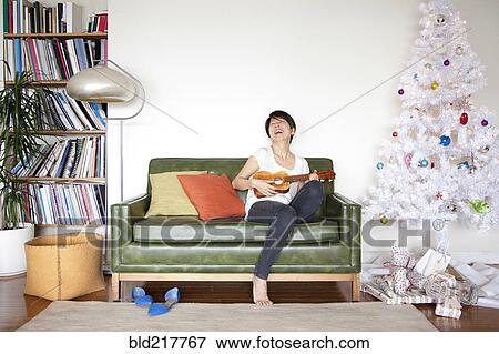 Stock Photo - Japanese woman playing ukulele near Christmas tree. Fotosearch