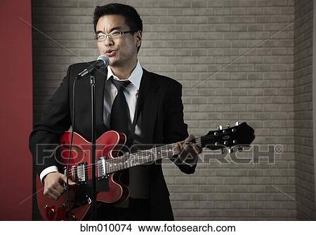 Korean man playing guitar and singing into microphone View Large Photo Image Picture - Korean man playing guitar and singing into microphone. Fotosearch