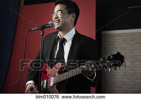 Stock Photograph - Korean man playing guitar and singing into microphone. Fotosearch