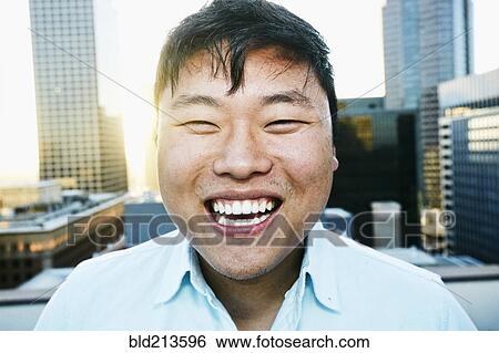 Stock Photograph - Korean man smiling on urban rooftop. Fotosearch