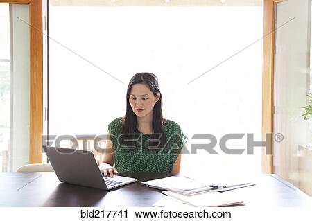 Stock Image - Korean woman paying bills on laptop. Fotosearch