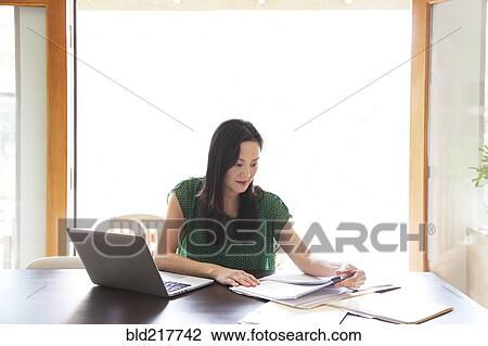 Stock Image - Korean woman paying bills on laptop. Fotosearch