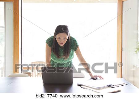 Stock Image - Korean woman using laptop in dining room. Fotosearch