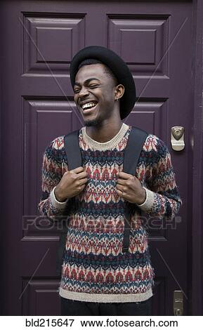 Laughing Black man wearing backpack near purple door View Large Photo Image Stock Photo - Laughing Black man wearing backpack near purple door. Fotosearch