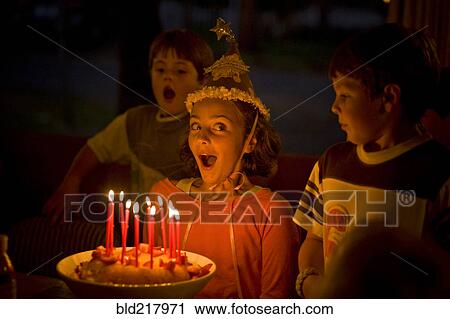 Stock Image - Laughing girl blowing candles on birthday cake. Fotosearch