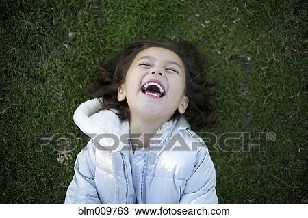 Stock Image - Laughing mixed race girl laying in grass. Fotosearch