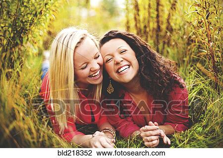 Stock Image - Laughing women laying together in tall grass. Fotosearch