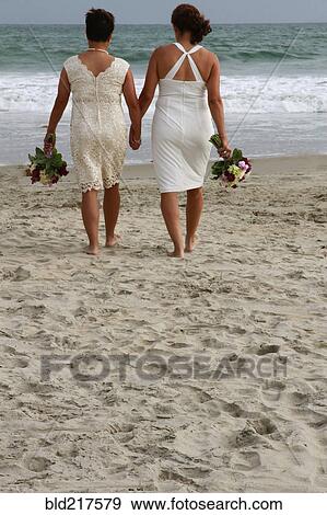 Stock Photo - Lesbian brides holding hands on beach. Fotosearch