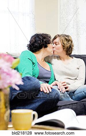 Stock Photo - Lesbian couple kissing on sofa in living room. Fotosearch