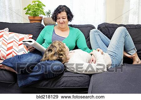 Stock Photo - Lesbian couple relaxing on sofa in living room. Fotosearch