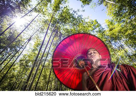 Stock Image - Low angle view of Asian monk-in-training under parasol in forest. Fotosearch