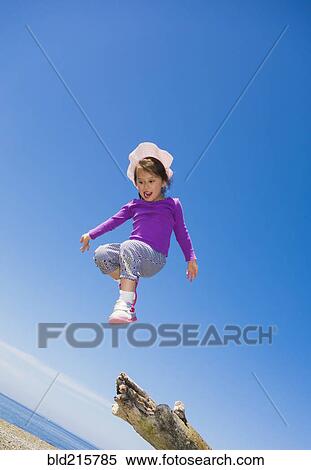 Stock Photography - Low angle view of mixed race girl jumping from log on beach. Fotosearch