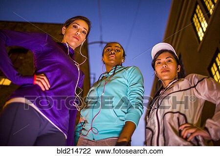 Stock Image - Low angle view of runners standing together at night. Fotosearch