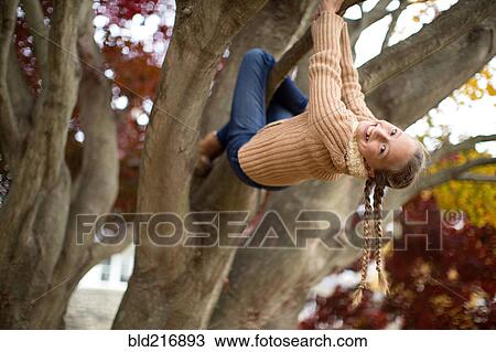 Stock Image - Low angle view of smiling girl climbing tree. Fotosearch