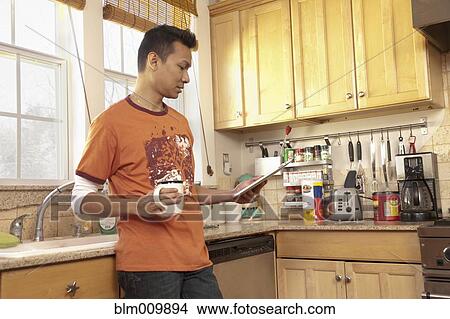 Picture - Malaysian man using digital tablet in kitchen. Fotosearch