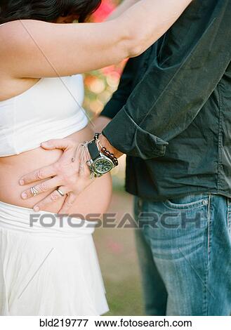 Stock Photo - Man holding belly of pregnant wife in backyard. Fotosearch