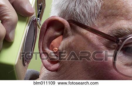 Stock Photo - Man putting speaker to hearing aid. Fotosearch