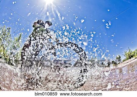Stock Photo - Man riding mountain bike through water. Fotosearch