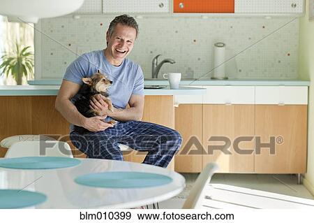 Stock Photo - Man sitting in kitchen with dog. Fotosearch