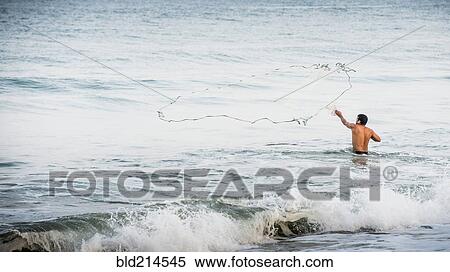 Stock Photography - Man throwing fishing net into ocean waves. Fotosearch
