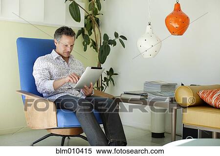 Man using digital tablet in living room View Large Photo Image Stock Photography - Man using digital tablet in living room. Fotosearch