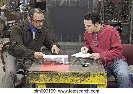 Stock Photo - Manager and worker reviewing paperwork in factory. Fotosearch
