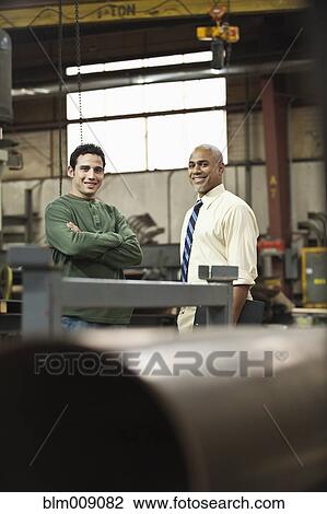 Stock Image - Manager and worker standing in factory. Fotosearch