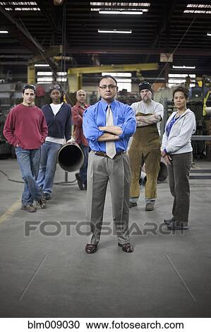 Stock Image - Manager and workers standing in factory. Fotosearch