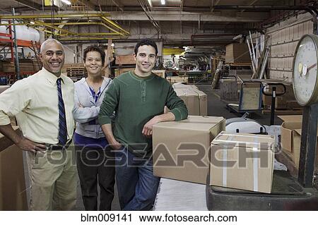 Stock Image - Manager and workers standing with boxed in factory. Fotosearch