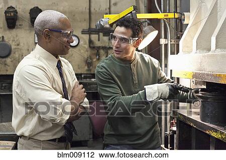 Stock Image - Manager talking to worker in factory. Fotosearch