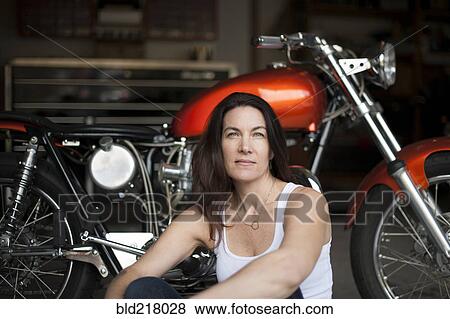 Stock Photo - Mechanic sitting with motorcycle in garage. Fotosearch