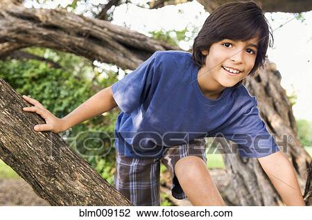Stock Image - Mixed race boy climbing tree. Fotosearch