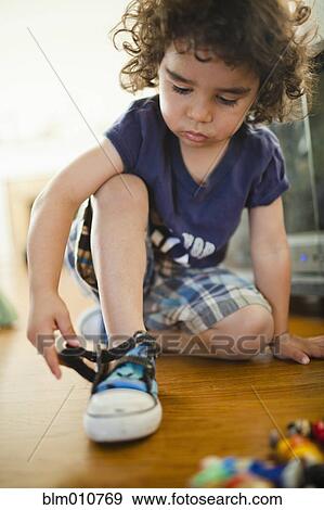 Stock Photo - Mixed race boy fastening shoes. Fotosearch