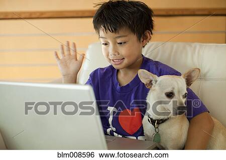 Stock Photograph - Mixed race boy using laptop and hugging dog. Fotosearch