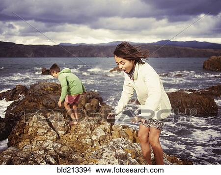 Picture - Mixed race brother and sister playing on rocky beach. Fotosearch