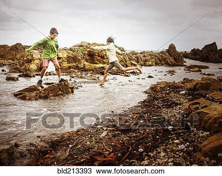 Stock Image - Mixed race brother and sister playing on rocky beach. Fotosearch