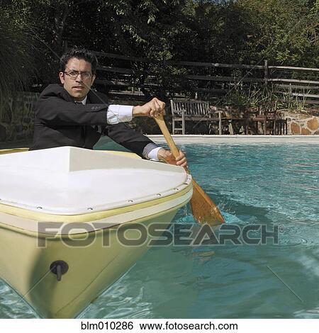 Stock Photograph - Mixed race businessman rowing boat in swimming pool. Fotosearch