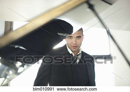 Stock Image - Mixed race businessman standing behind piano. Fotosearch
