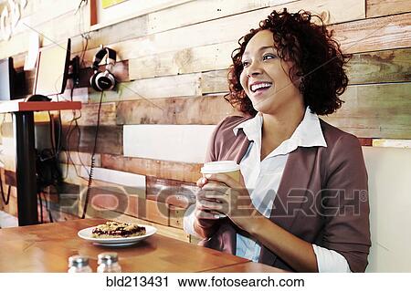 Stock Image - Mixed race businesswoman having coffee and pastry in cafe. Fotosearch