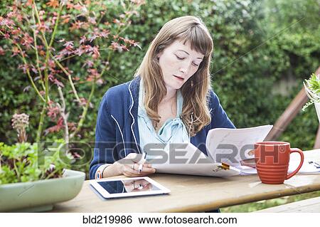 Stock Photograph - Mixed race businesswoman reading paperwork in backyard. Fotosearch