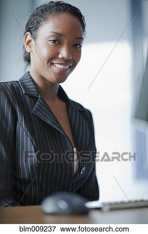 Stock Photo - Mixed race businesswoman sitting at desk. Fotosearch