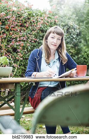 Stock Image - Mixed race businesswoman writing notes in backyard. Fotosearch
