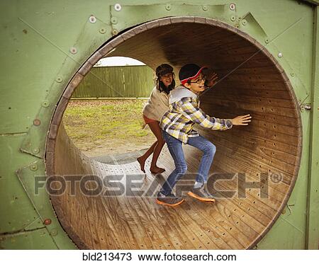 Stock Image - Mixed race children playing in wheel in playground. Fotosearch