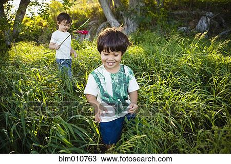 Stock Image - Mixed race children walking through tall grass. Fotosearch